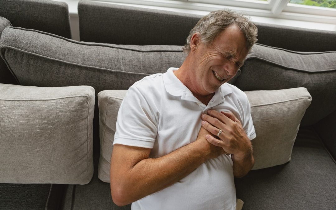 Active senior Caucasian man suffering from chest pain on sofa in a comfortable home